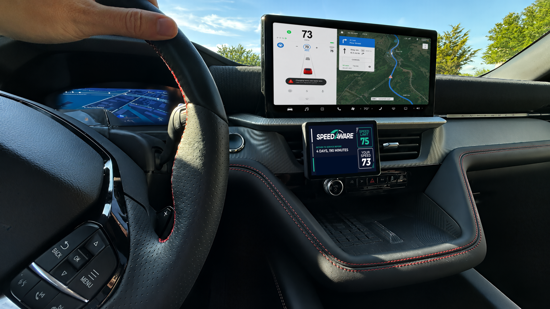 Interior of car with two screens and a persons hand holding the driving wheel.